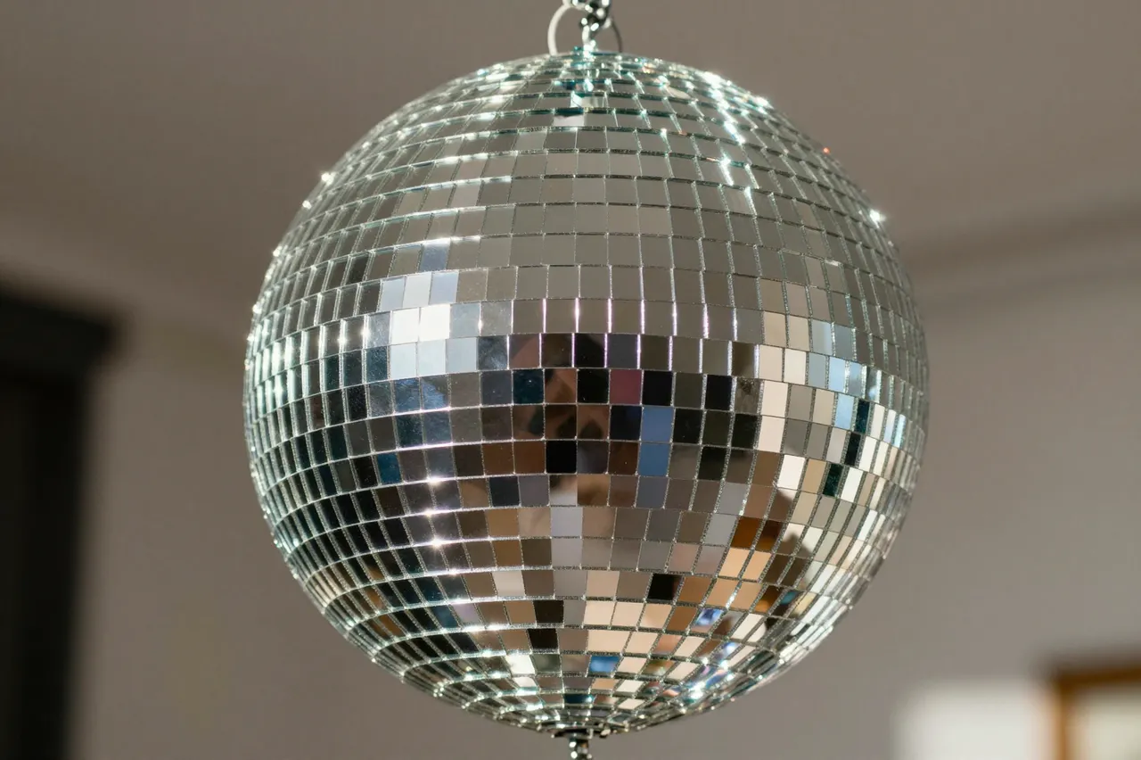 A close-up of a reflective mirrored disco ball suspended from a ceiling, catching bright glints of light