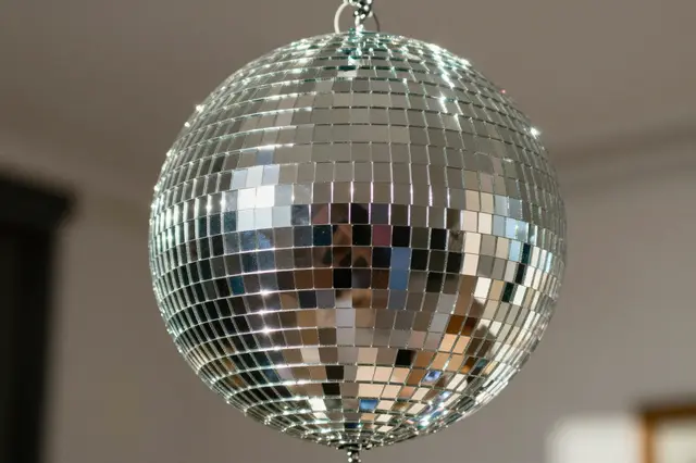 A close-up of a reflective mirrored disco ball suspended from a ceiling, catching bright glints of light
