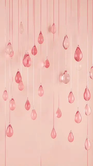 Translucent pink blown-glass teardrop shapes hang from thin strings against a soft blush background