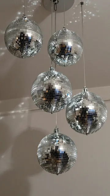 Five mirrored silver disco balls hang from a ceiling casting scattered light spots on a neutral wall