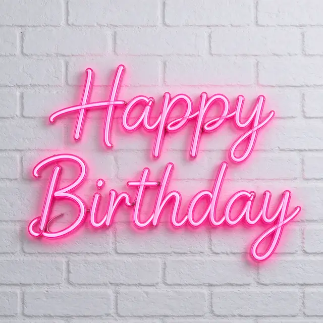 Bright pink neon 'Happy Birthday' script sign glowing on a white painted brick wall
