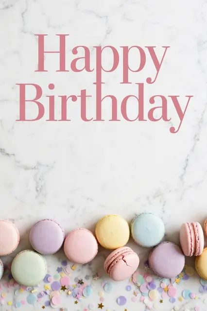 "Happy Birthday" in rose pink serif type above pastel macarons and scattered confetti on a white marble surface