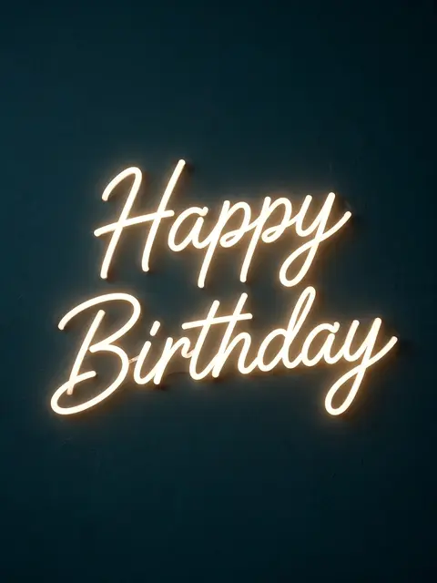 Warm white neon script reading "Happy Birthday" glows against a dark teal textured wall