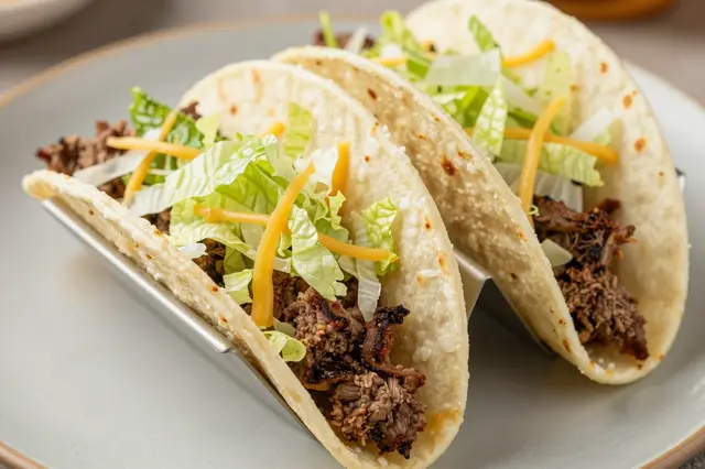 Two hard shell beef tacos with shredded lettuce and cheddar rest in a metal taco holder on a gray plate