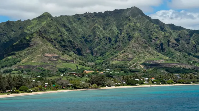 Lush green volcanic mountains rise above a turquoise ocean bay and sandy shore in Hawaii