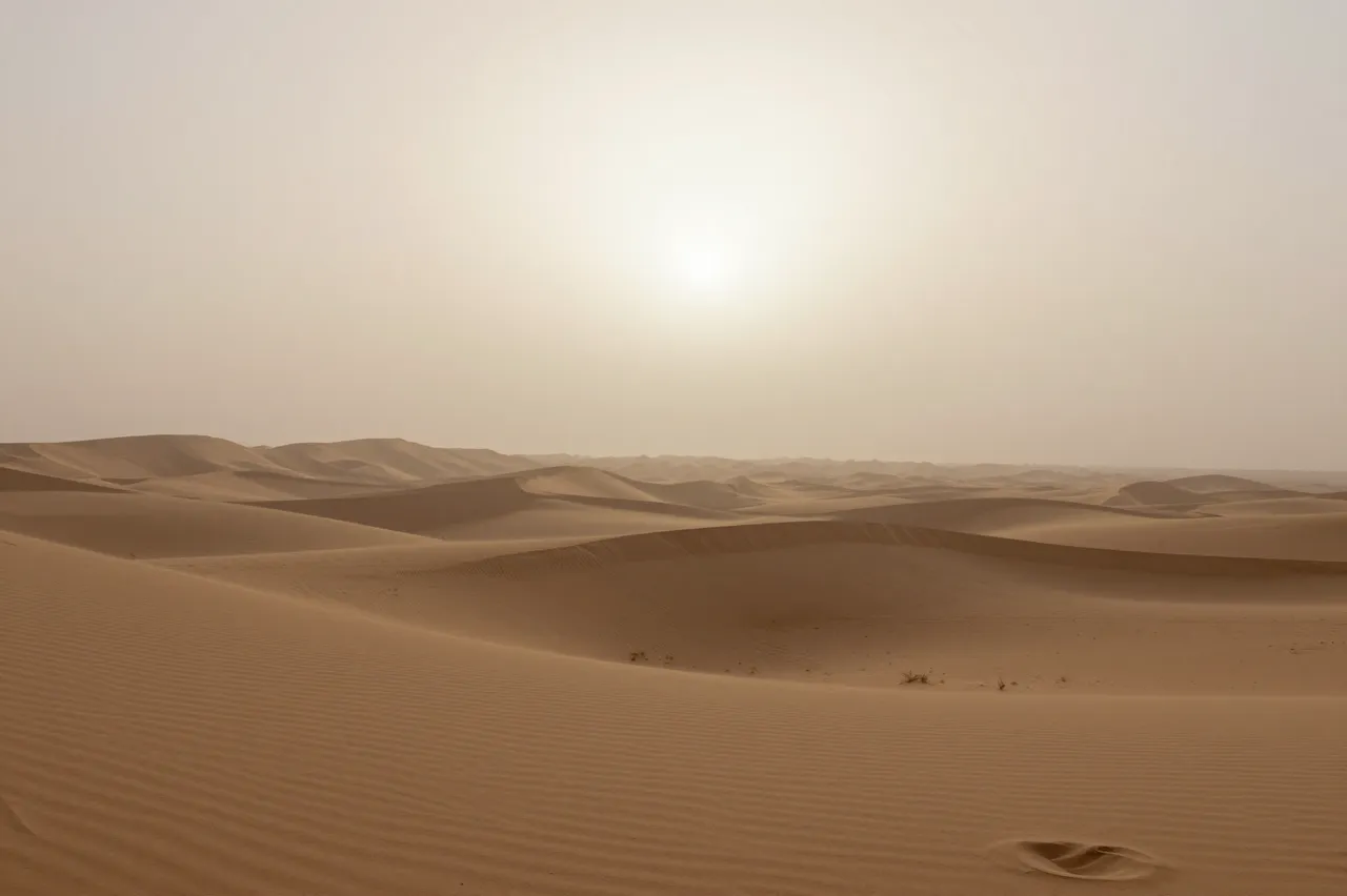 Pale sun shines through sandstorm haze over rolling desert sand dunes