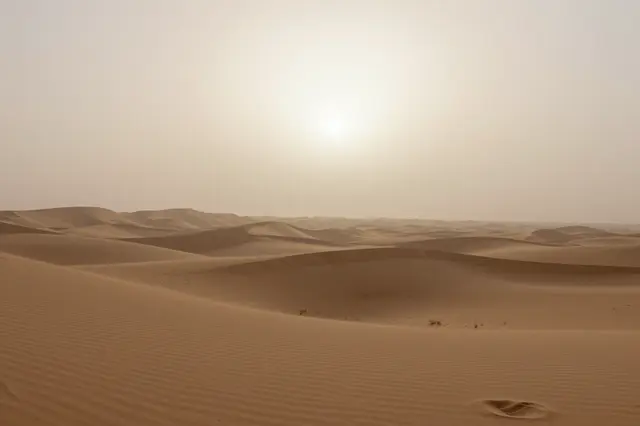 Pale sun shines through sandstorm haze over rolling desert sand dunes