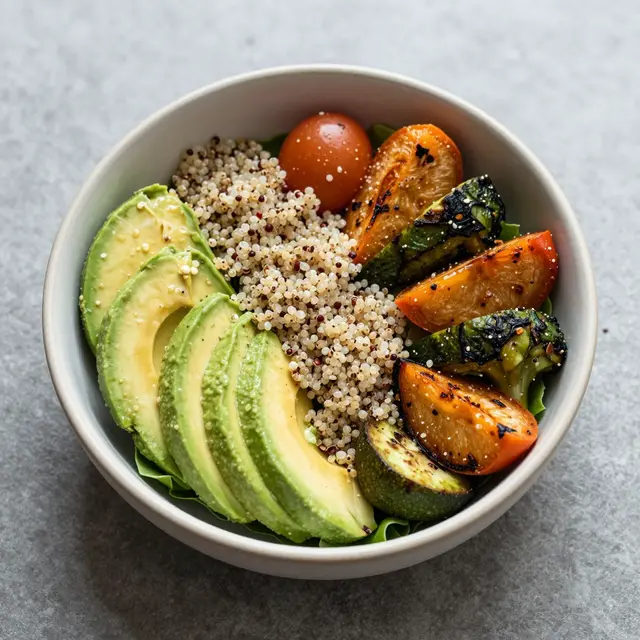 Overhead view of a salad bowl filled with avocado, quinoa, and grilled vegetables on a gray countertop
