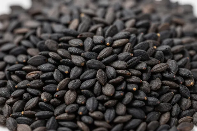 Macro close-up of a dense pile of whole black sesame seeds with shallow depth of field