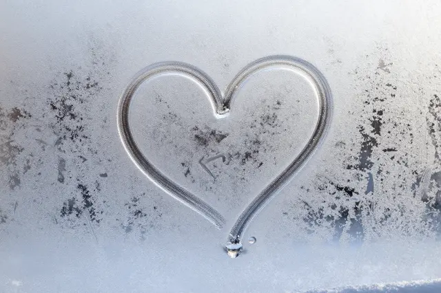 A hand-drawn heart etched into the frosty condensation of a cold window pane