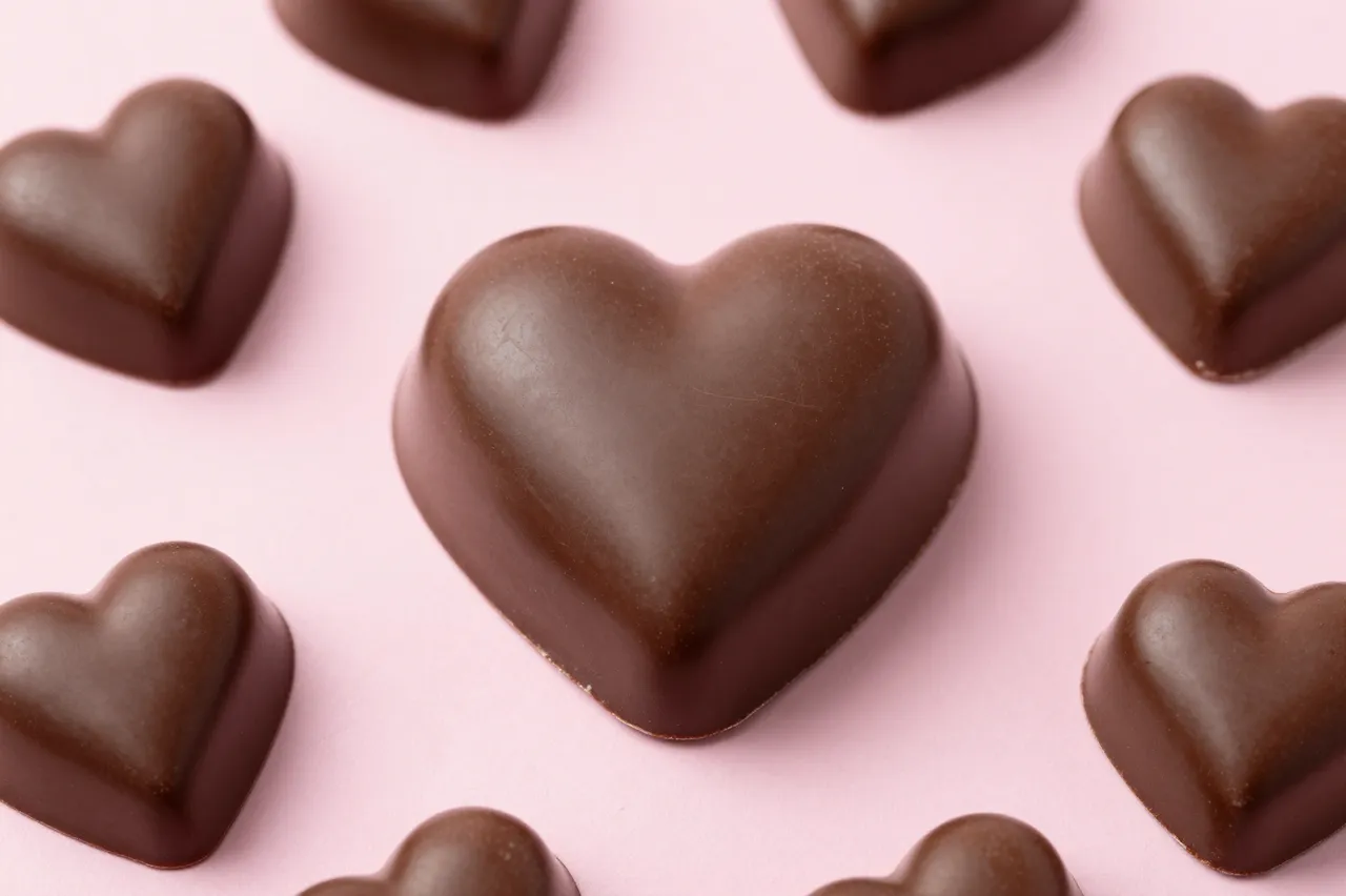 Top-down view of glossy heart-shaped chocolates arranged on a smooth soft pink background