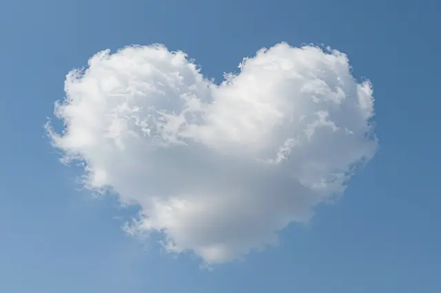 A fluffy heart-shaped white cloud floats against a clear bright blue sky.