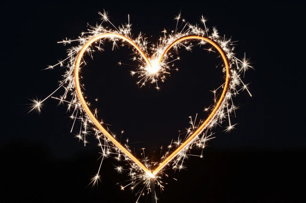 A lit sparkler forms a glowing heart shape against a dark night sky