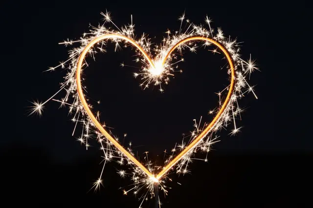 A lit sparkler forms a glowing heart shape against a dark night sky