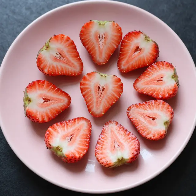 Top-down view of sliced heart-shaped strawberry halves arranged on a pale pink plate over a dark surface