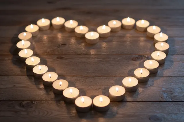Lit tealight candles arranged in a neat heart shape rest on dark wooden planks at night