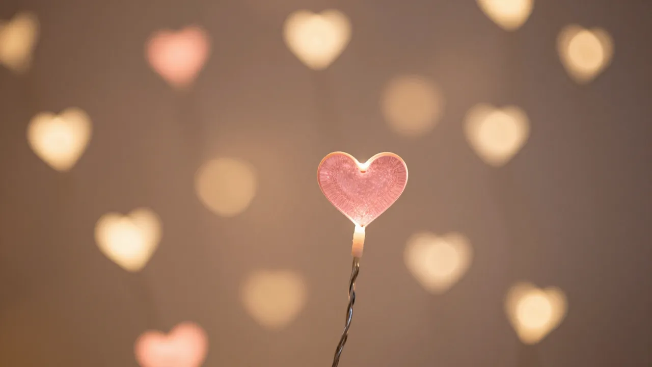 A sharp pink heart fairy light sits in front of soft blurred rose and gold heart-shaped bokeh lights