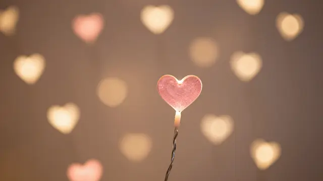 A sharp pink heart fairy light sits in front of soft blurred rose and gold heart-shaped bokeh lights