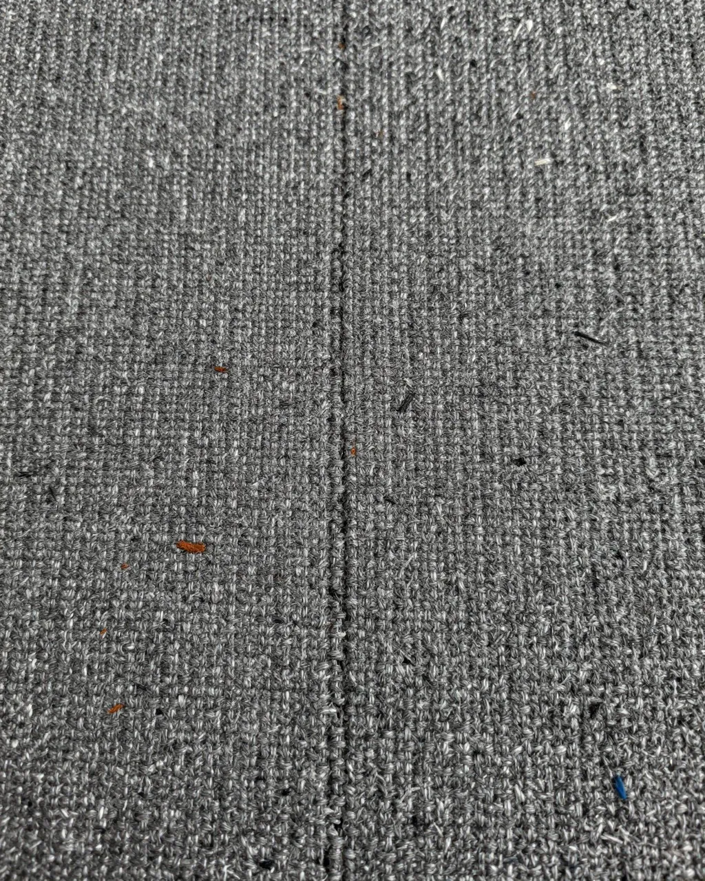 Full frame close-up of heather gray tweed fabric with coarse weave and scattered blue and rust flecks