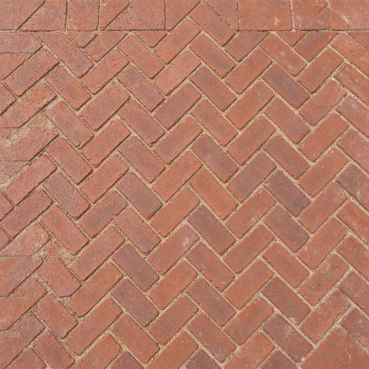 Top view full frame of red clay bricks laid in a tight herringbone pattern with sandy mortar joints
