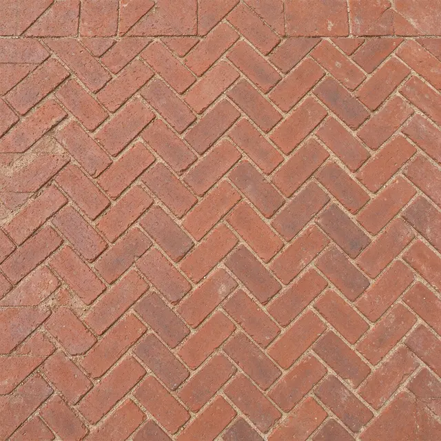 Top view full frame of red clay bricks laid in a tight herringbone pattern with sandy mortar joints