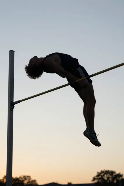 A high jumper arches over the high jump bar against a soft gradient evening sky