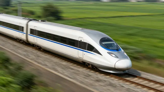 White and blue high-speed train travels on railway tracks past blurred green countryside.