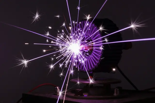 A high voltage coil discharges bright purple and white sparks against a dark room background