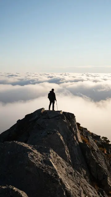 Silhouetted hiker stands on a rocky mountain peak overlooking a sea of clouds at dawn