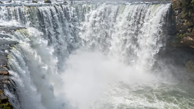 A wide horseshoe-shaped cascade of water crashes down, with thick white mist rising from the base.