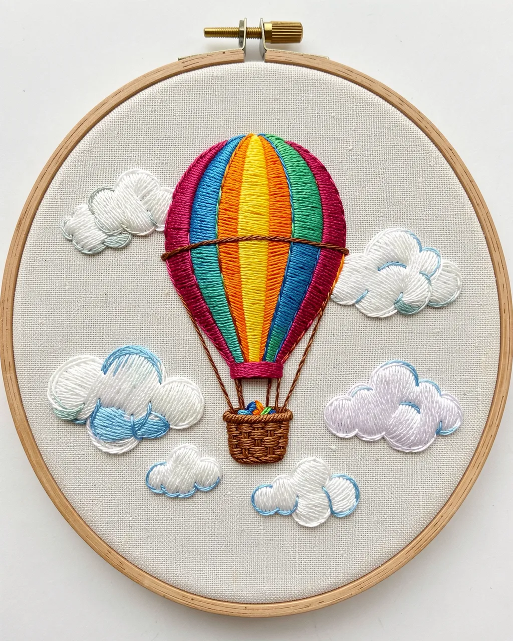 Stitched multicolor hot air balloon and clouds displayed in a wooden embroidery hoop on linen