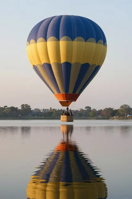 Colorful hot air balloon floating low over a still calm lake with its full reflection visible at dawn