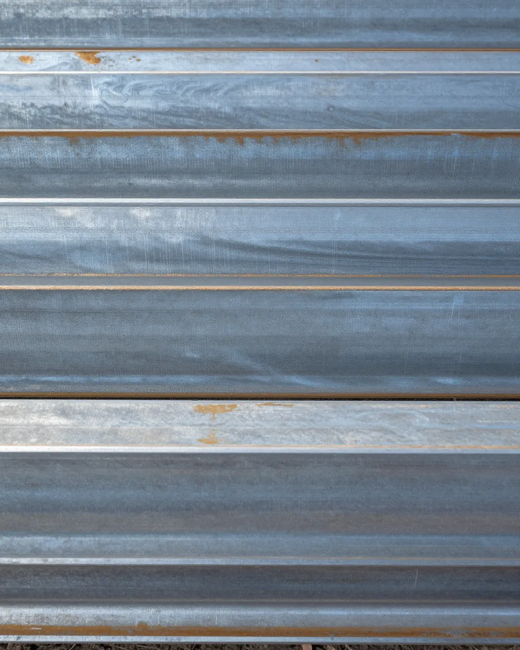 Full frame close-up of stacked blue-gray hot-rolled steel with faint mill swirls and light rust edge traces under flat