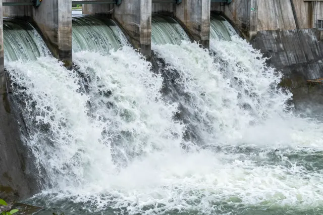 Turbulent water rushes through the open spillway gates of a concrete hydroelectric dam.