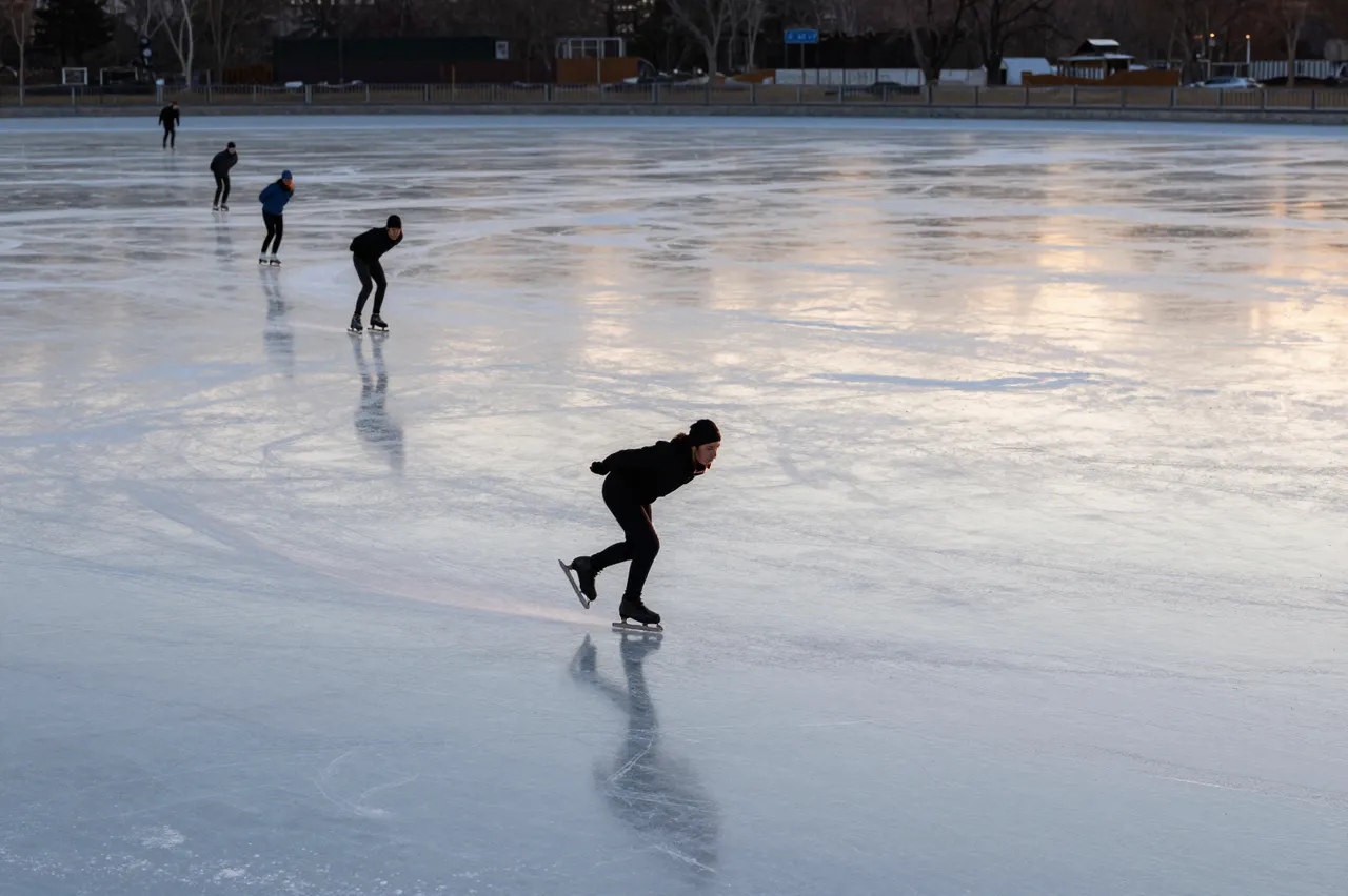 Group of speed skaters gliding across a smooth frozen pond at golden sunset, seen from a distance.