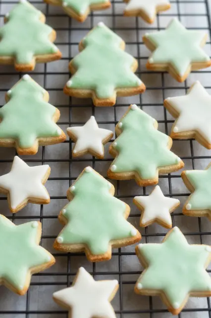 Tree and star shaped sugar cookies with pale green and white royal icing rest on a black wire cooling rack.