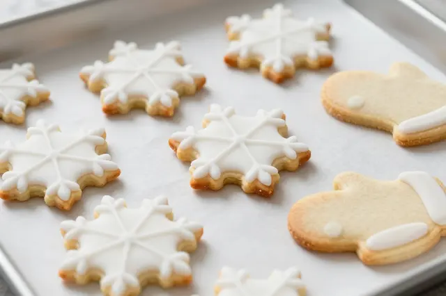 Snowflake and mitten shaped iced sugar cookies rest on parchment lined baking tray