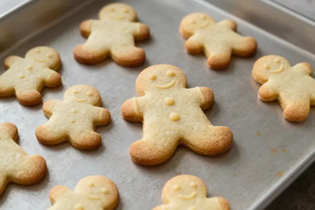 Smiling gingerbread man shaped cookies rest arranged on a metal baking sheet