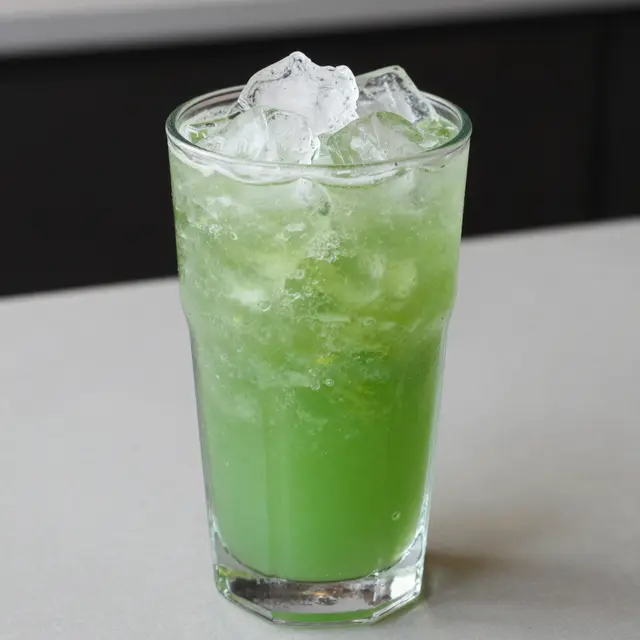 Tall glass of bright green blended iced mint lemonade with crushed ice on a light countertop