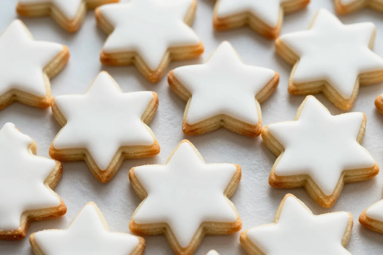 Star-shaped sugar cookies with smooth white icing rest on parchment paper in an even pattern
