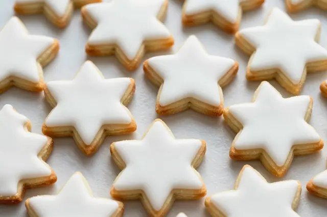 Star-shaped sugar cookies with smooth white icing rest on parchment paper in an even pattern