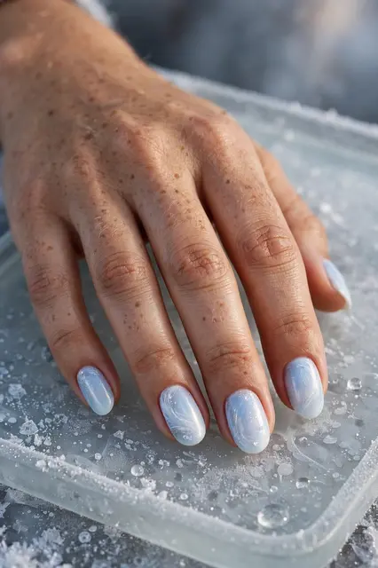 A woman's hand with pale blue icy gradient manicure rests on a frosted glass tray