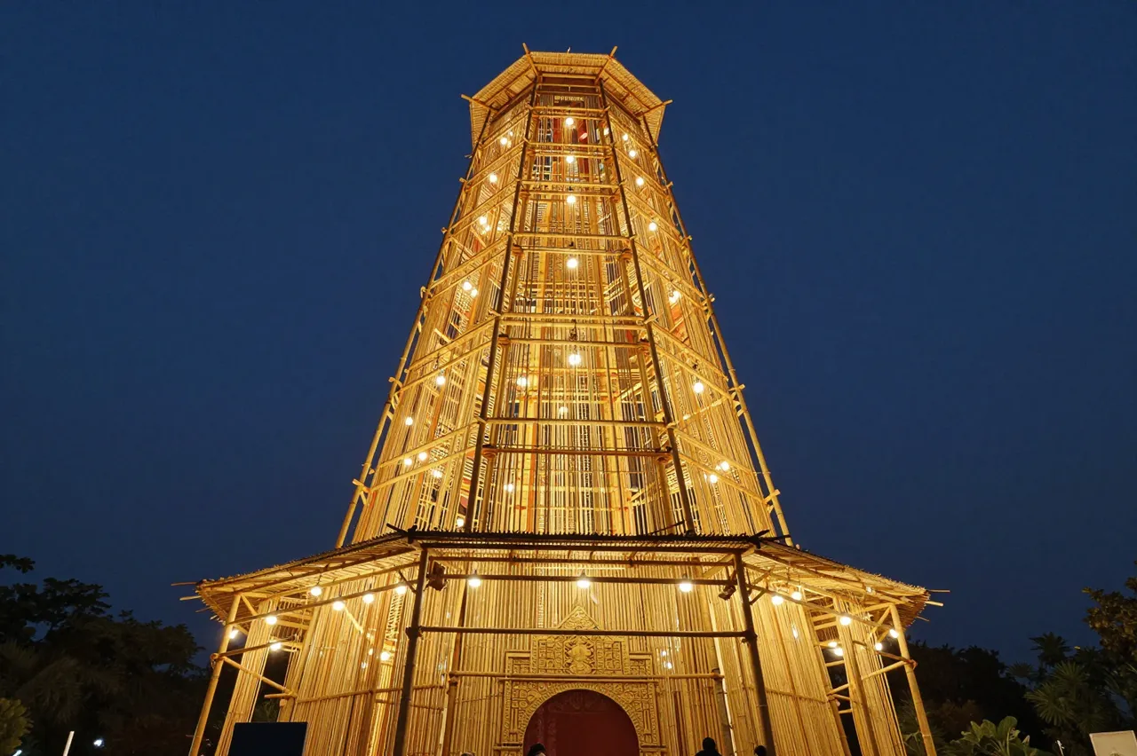 Tall glowing bamboo festival structure lit with warm lights under a dark evening sky