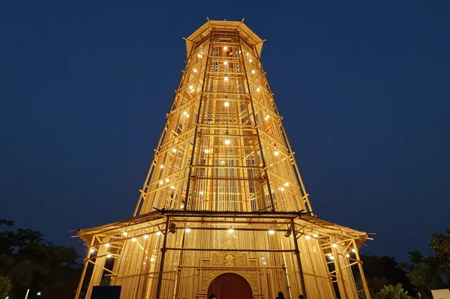 Tall glowing bamboo festival structure lit with warm lights under a dark evening sky