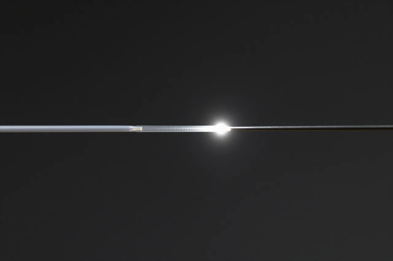A macro shot of a fiber optic strand with a bright glowing point of light against a dark black background