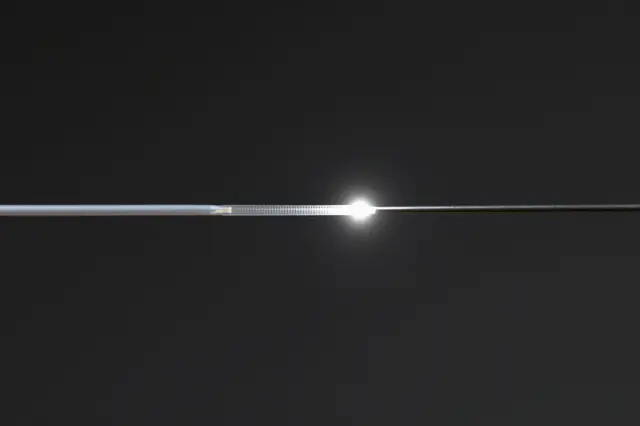A macro shot of a fiber optic strand with a bright glowing point of light against a dark black background