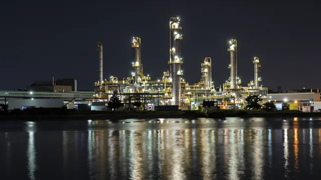Lights from a petrochemical refinery reflect on still canal water under a dark night sky