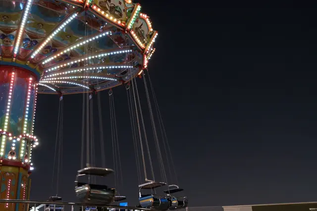 Lit amusement park swing ride with motion blur against a dark night sky