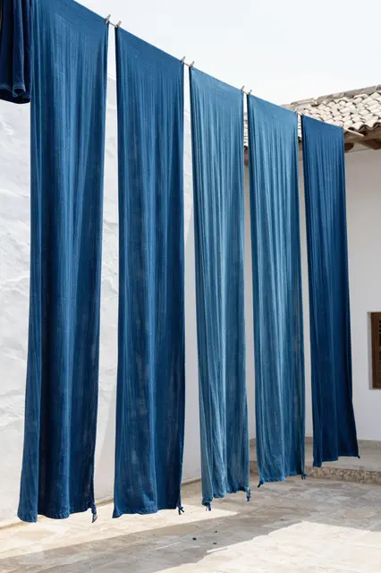 Long lengths of indigo dyed fabric hang to dry from a line in a sunny whitewashed courtyard