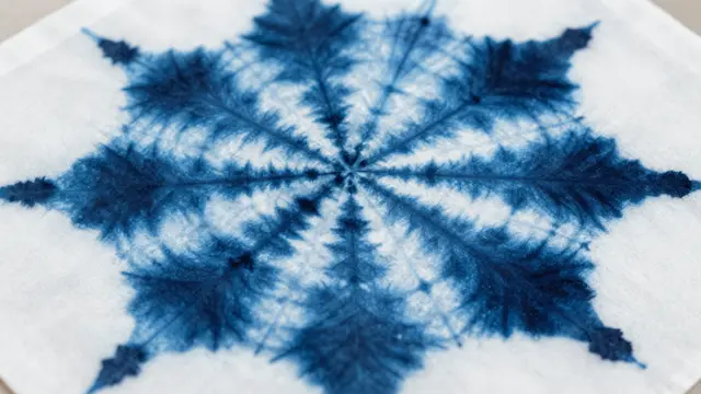 Symmetrical radial indigo shibori dye pattern spread across a plain white woven cloth